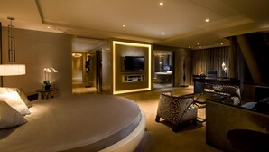 Una habitación de hotel moderna con una cama grande, televisión, zona de estar con sillas estampadas y una mesita con lámpara.