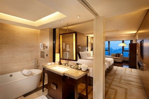 Un baño de hotel moderno con bañera, dos lavamanos, un espejo grande y vistas a la ciudad a través de amplias ventanas.