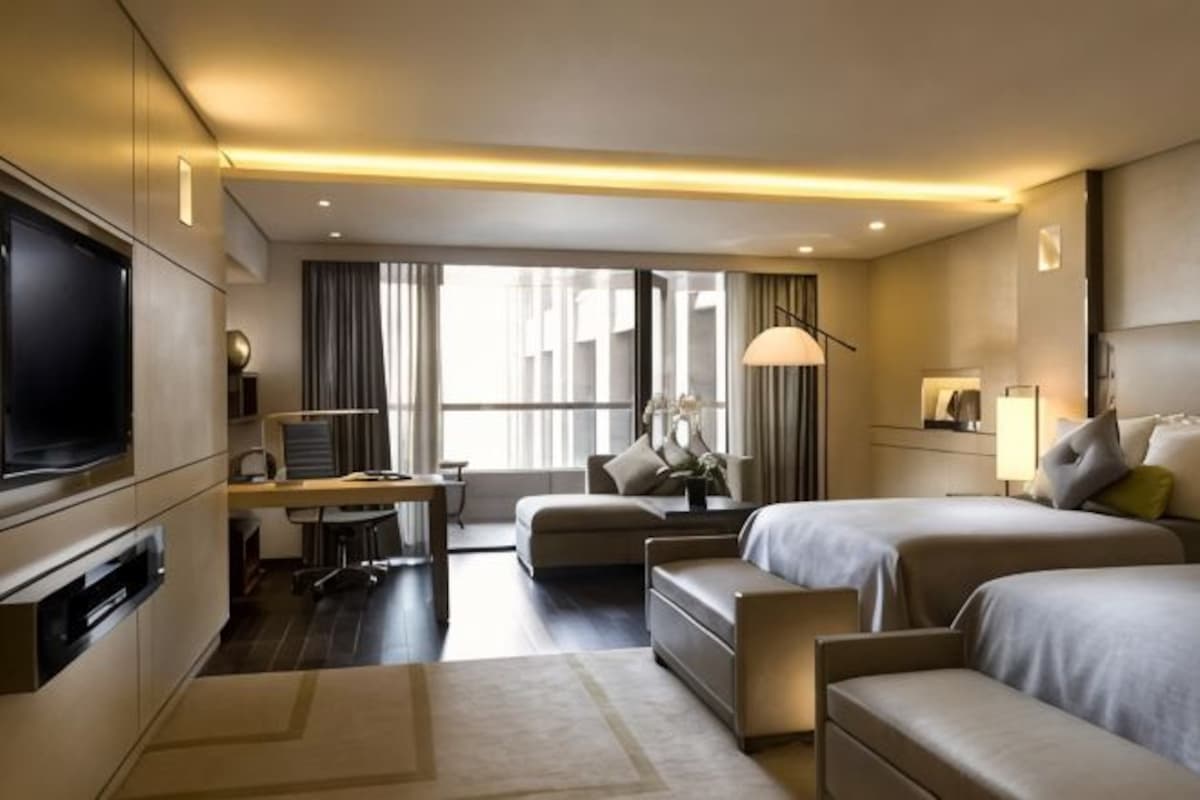 Une chambre d’hôtel équipée d’une télévision, d’un bureau, de deux lits, d’un canapé et d’une grande fenêtre.