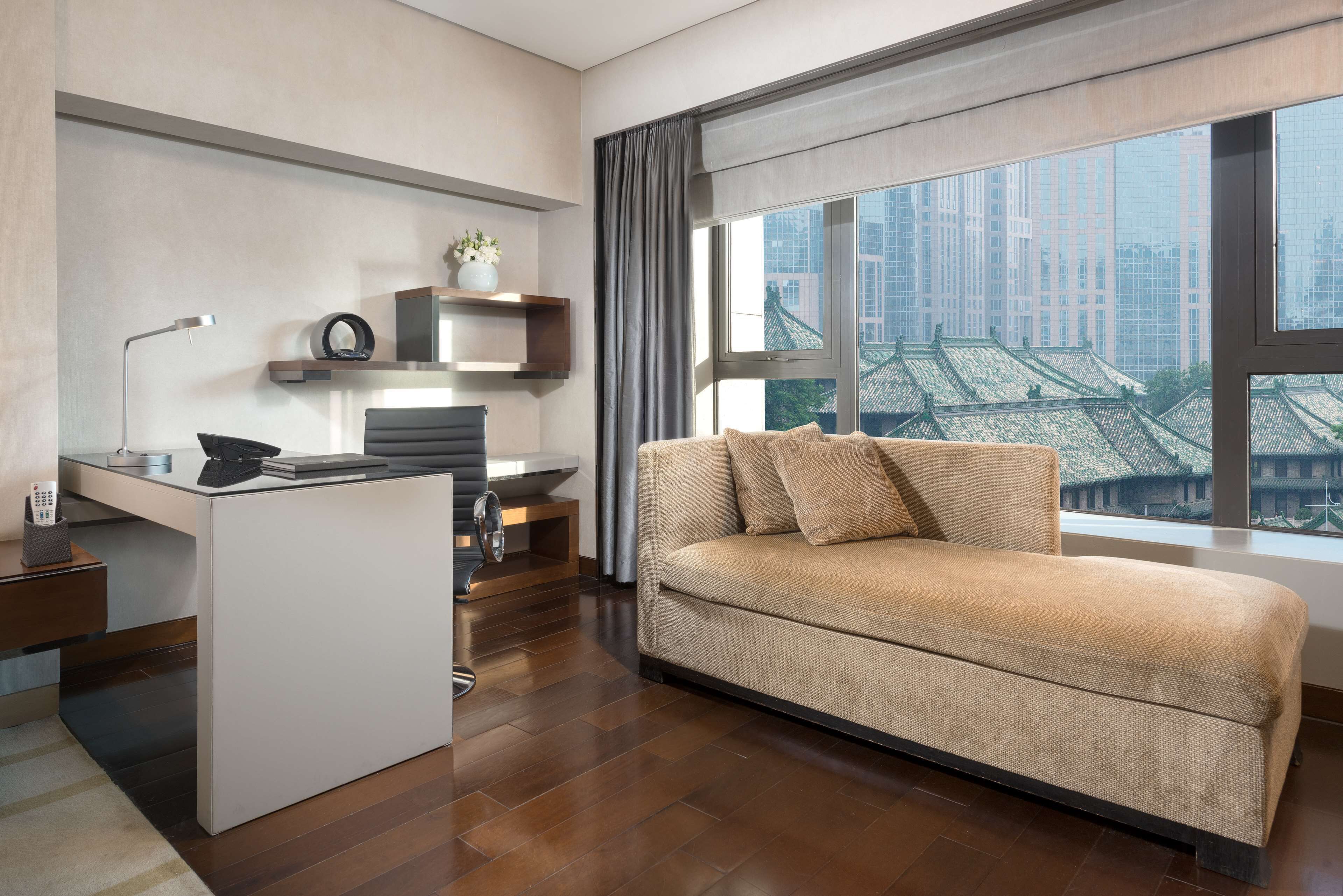 A modern living room with a sofa, a desk, and a large window with a city view.