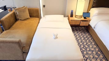 A hotel room with a bed, a sofa, a nightstand with a lamp, and a wall-mounted TV.