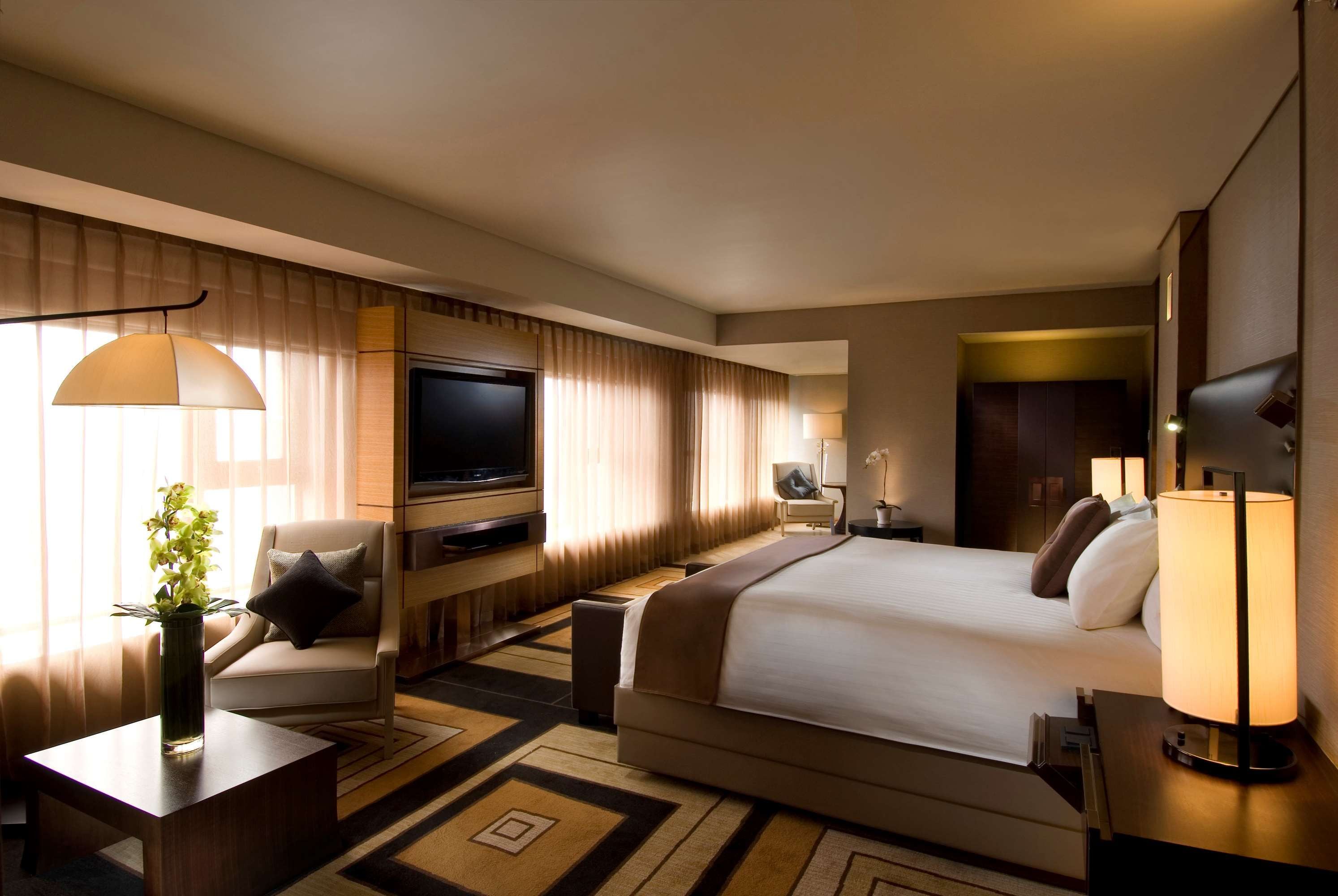 Una habitación de hotel con una cama, televisión, escritorio, silla y lámpara.