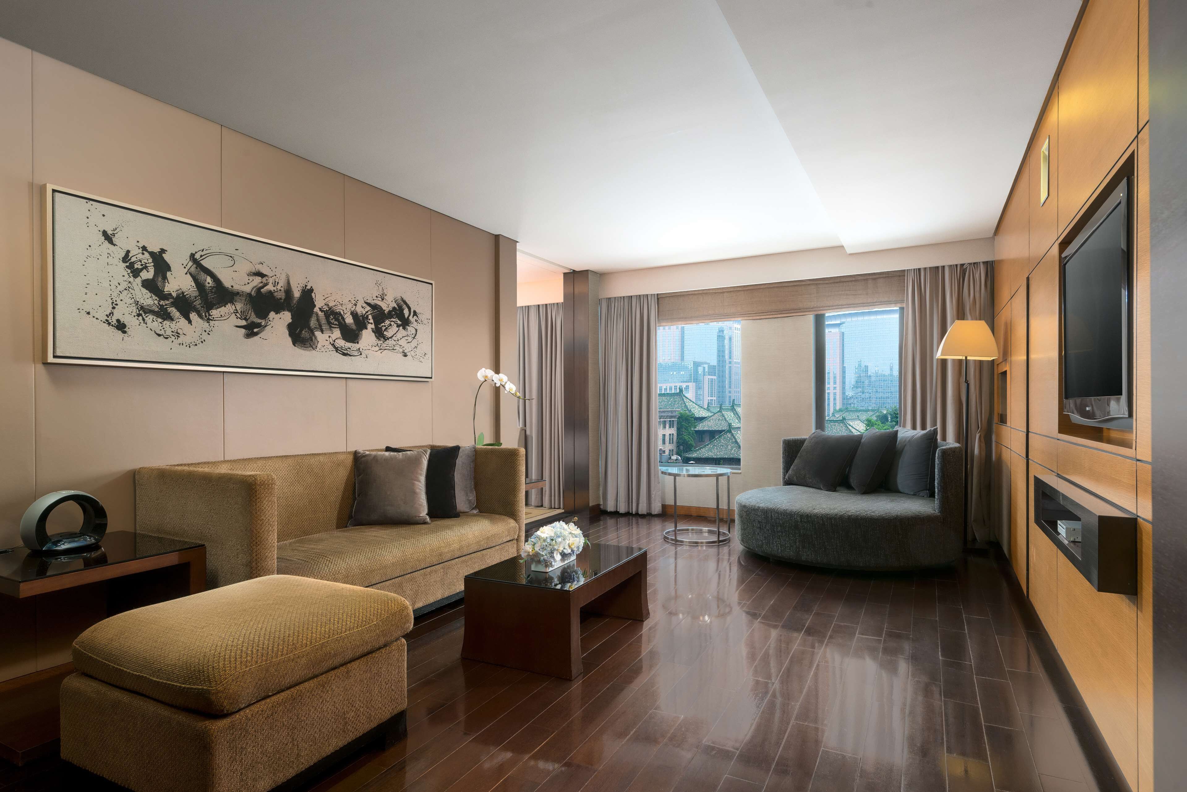 A modern hotel room with a large abstract painting, two sofas, a coffee table, and a TV.