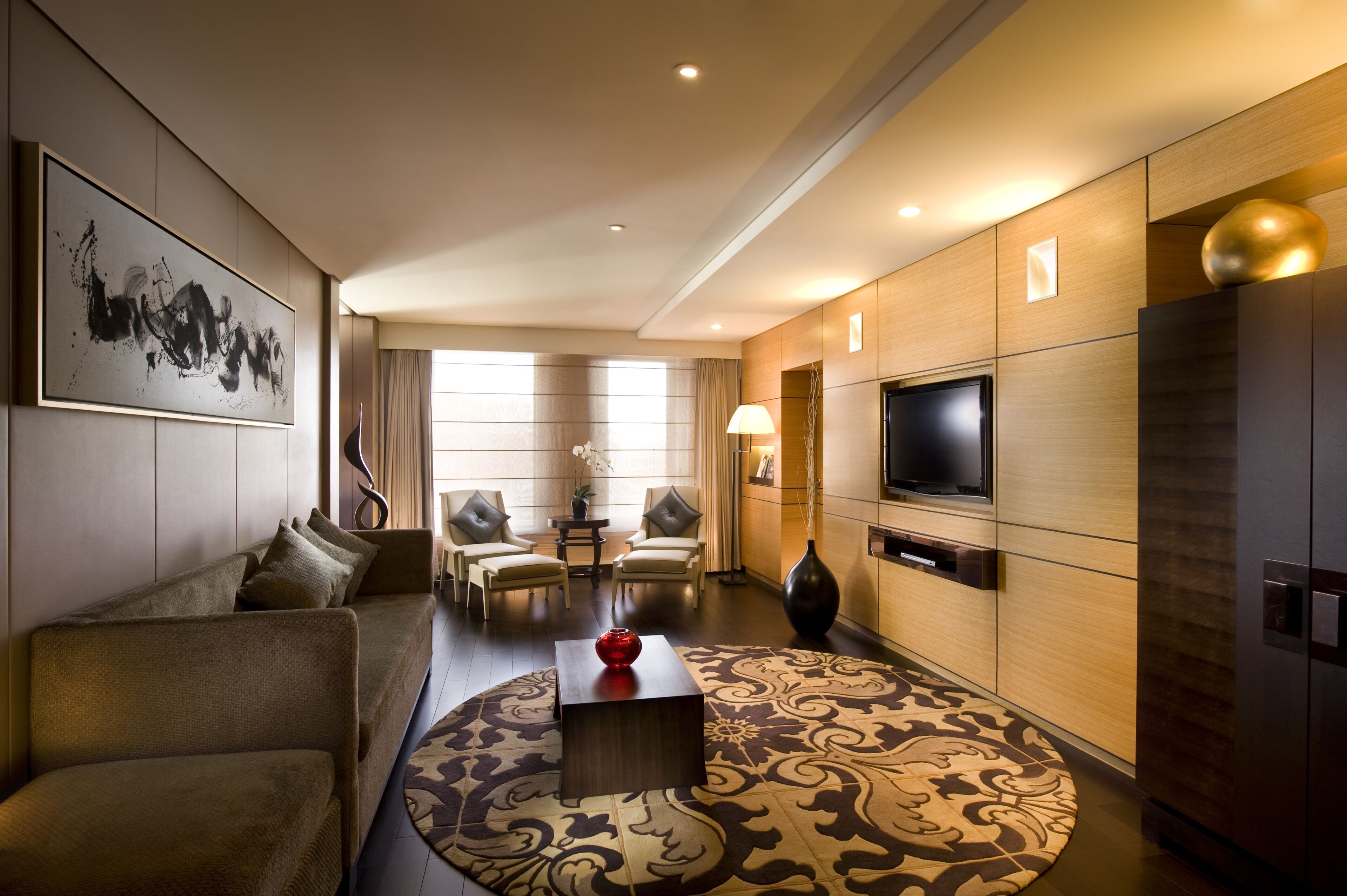 Een moderne hotelkamer met een bank, stoelen, een televisie en een decoratieve vaas.