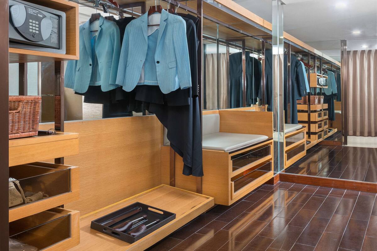 A modern hotel room with a wooden vanity, a mirror, a seating area, and a clothing rack with various garments.