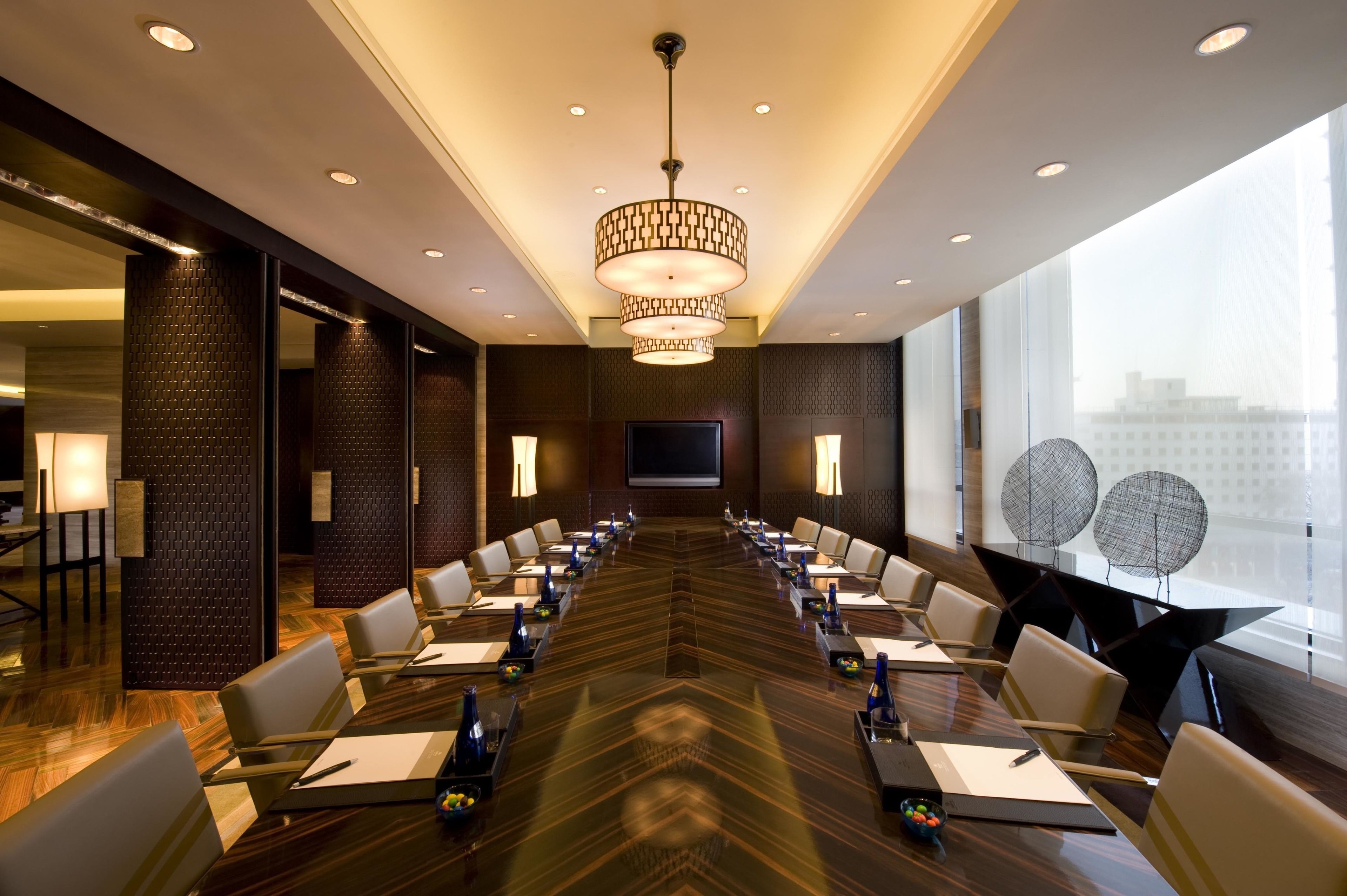 A conference room with a long table, chairs, a large screen, and a modern chandelier.