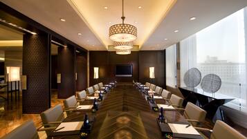 A conference room with a long table, chairs, a large screen, and a modern chandelier.