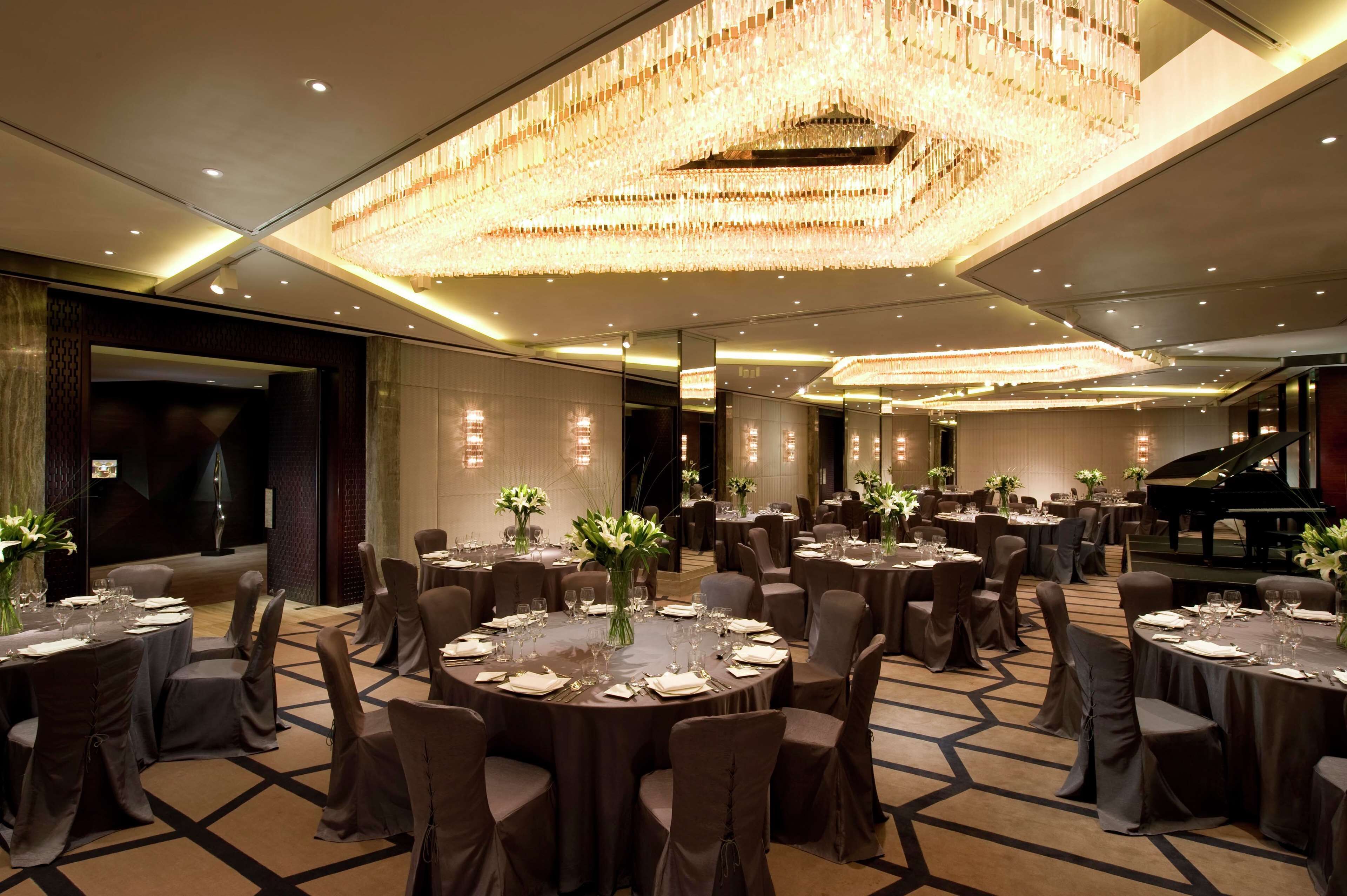 A banquet hall with round tables, chairs, and a grand chandelier.