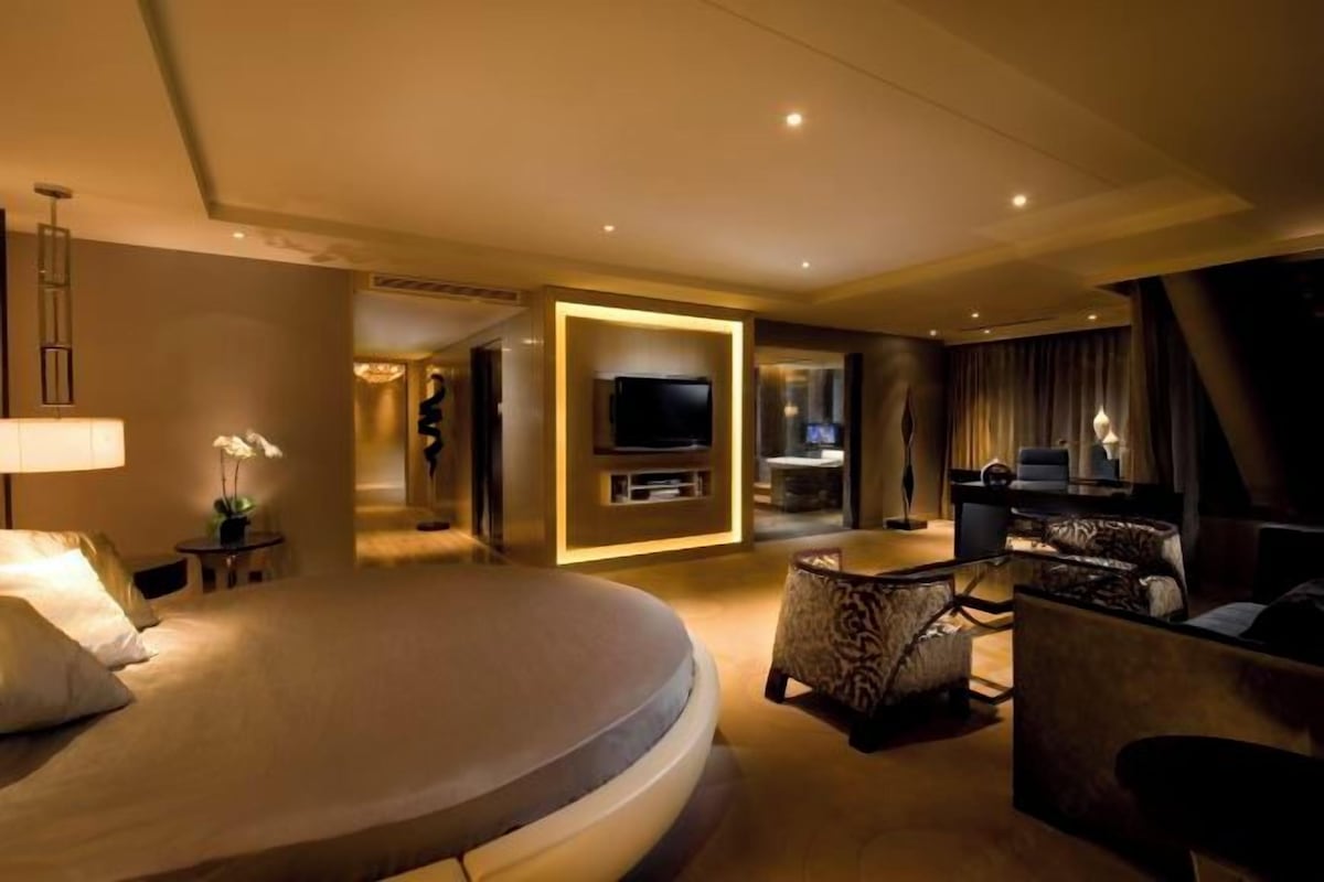 A modern hotel room with a large bed, a television, a seating area with patterned chairs, and a small table.