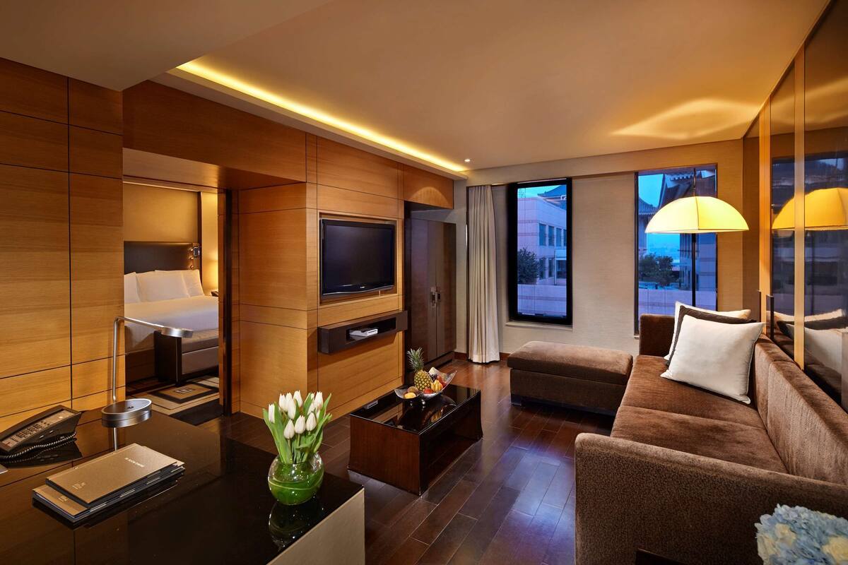 A modern hotel room with a bed, TV, sofa, and coffee table.