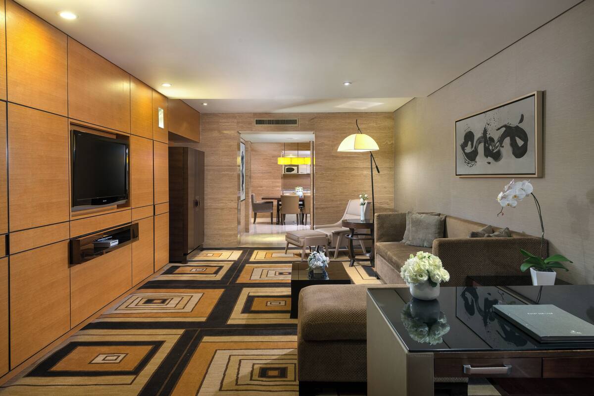 A modern living room with a flat-screen TV, a sofa, a coffee table, and a dining area in the background.