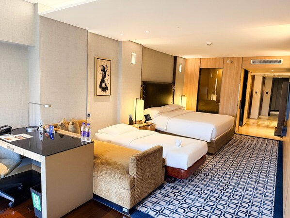 Habitación de hotel con escritorio, dos camas, una silla, un cesto de basura y piso con estampado.