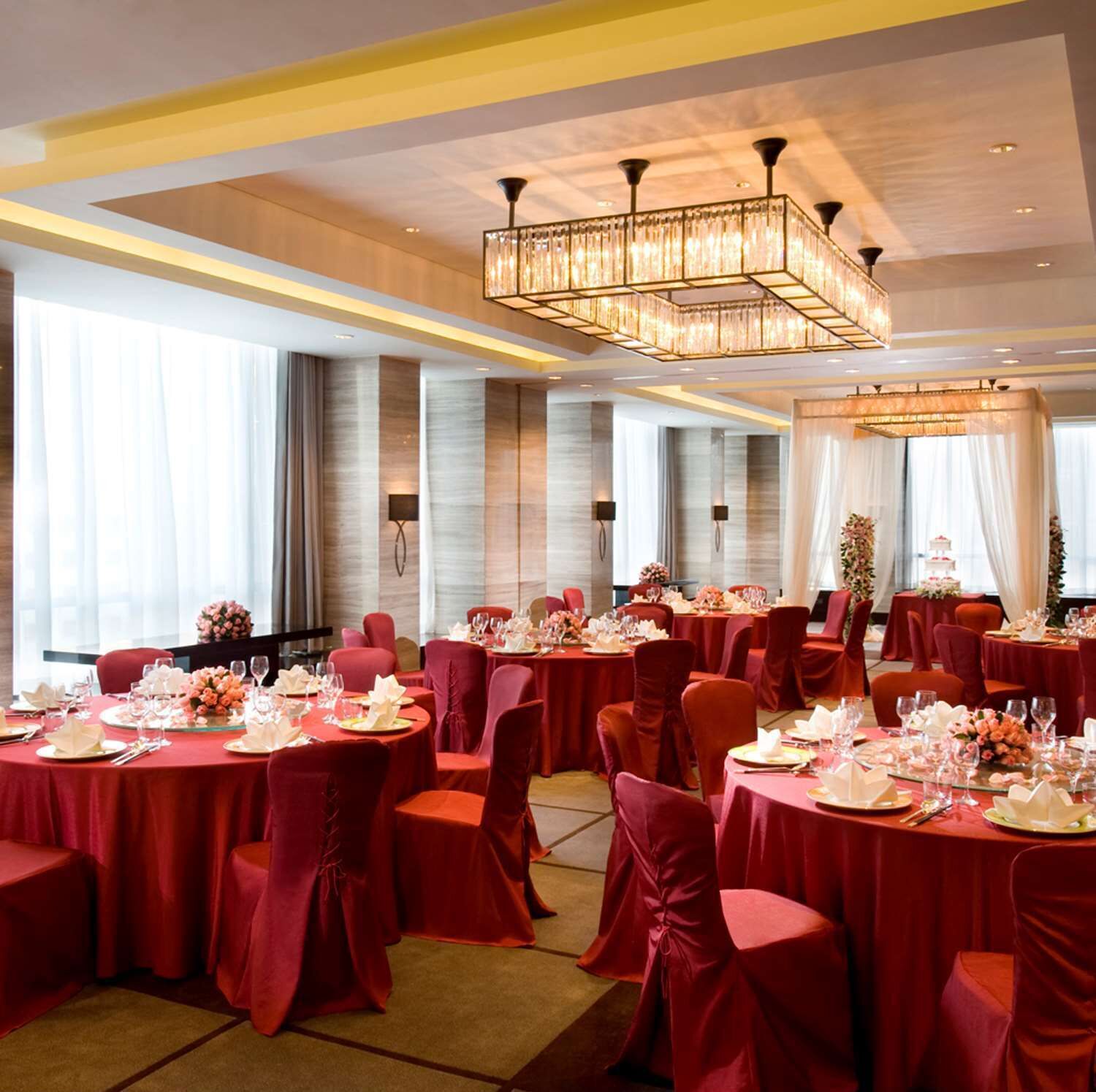 Un salón de banquetes con mesas redondas, manteles rojos y sillas a juego.