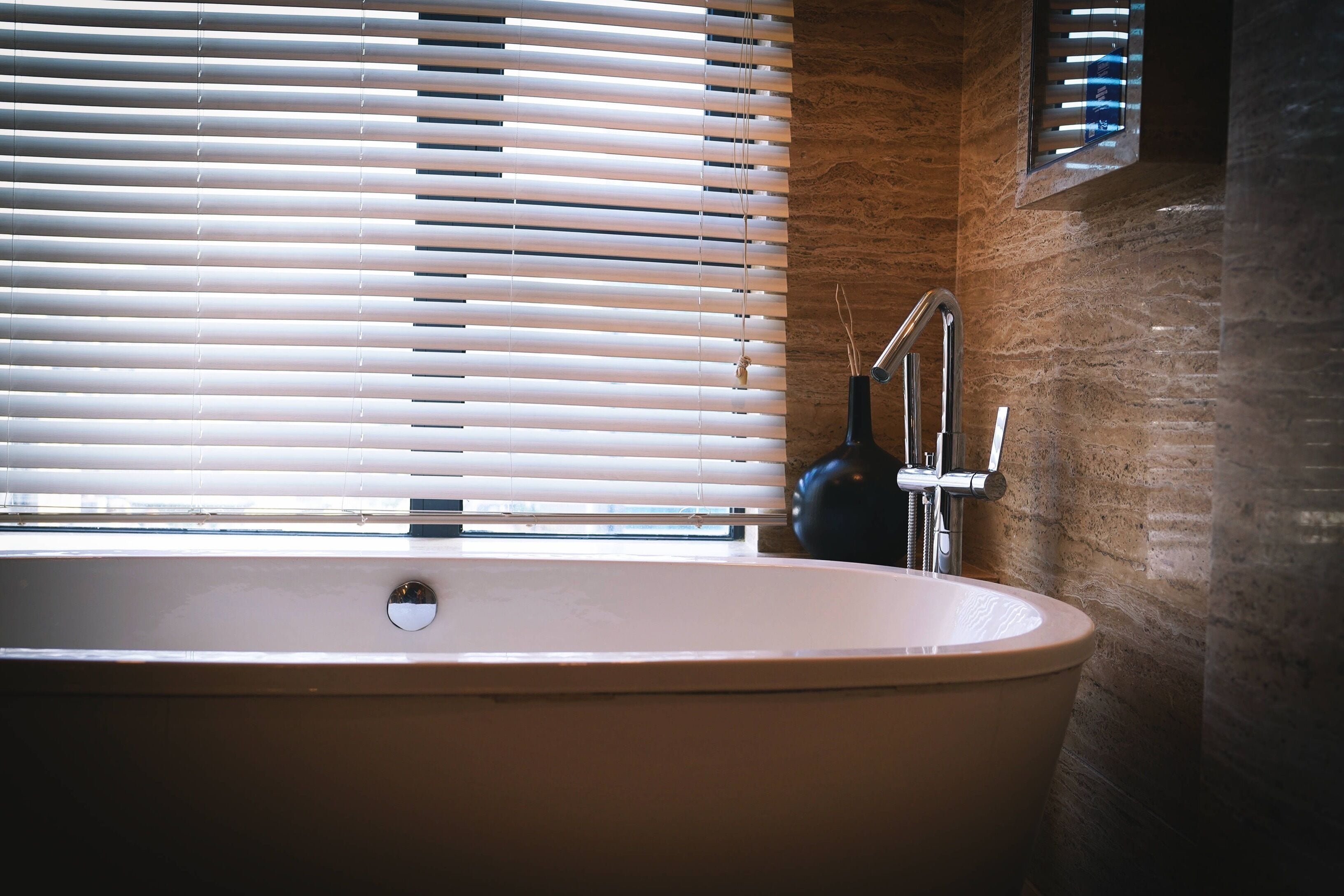 A bathroom with a freestanding bathtub, a window with blinds, and a wall-mounted towel rack.