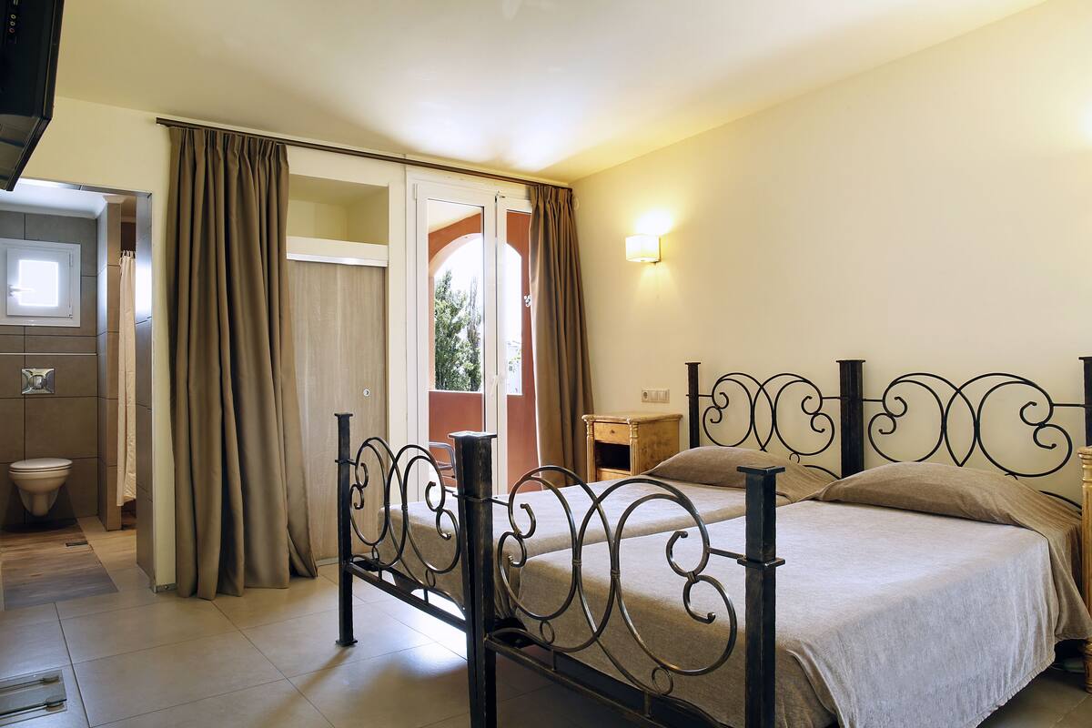 A bedroom with a bed, curtains, a nightstand, and a bathroom visible through an open door.