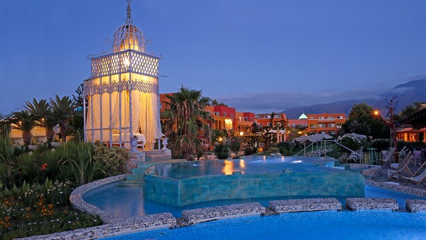 A resort pool area with a large, ornate gazebo, palm trees, and a mountain backdrop. - Orpheas Resort - Adults Only (Apokoronas)
