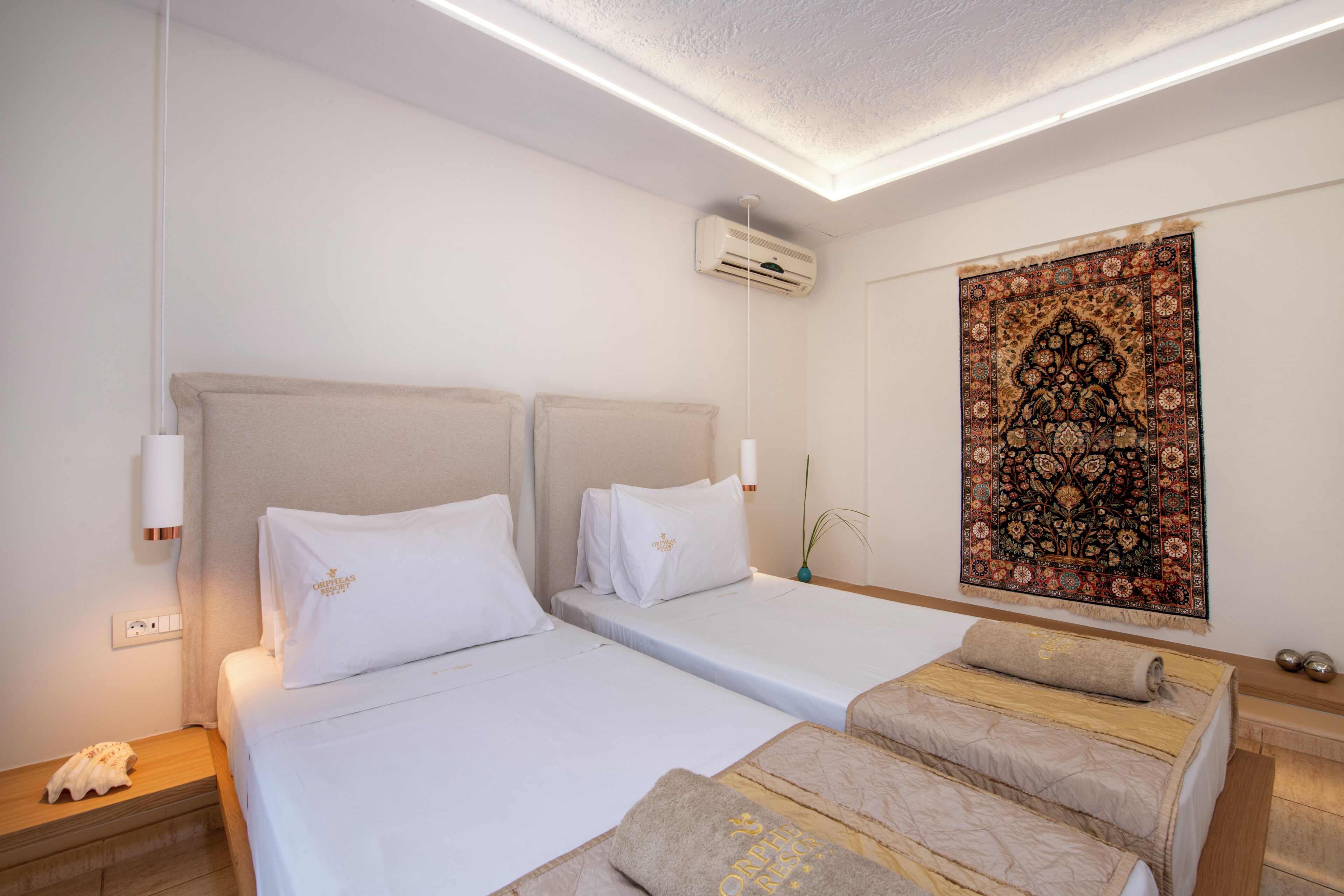 A hotel room with two beds, a large decorative tapestry, and an air conditioning unit.