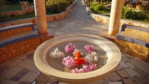 A stone fountain with flowers in a garden pathway. - Orpheas Resort - Adults Only (Apokoronas)
