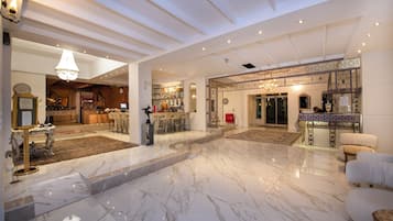 Un vestíbulo amplio con piso de mármol, un área de bar y un espacio de descanso con sillas y un sofá.