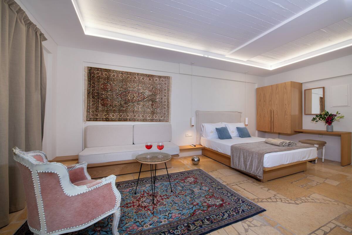 A modern bedroom with a large bed, a sofa, a small table with two glasses, and a decorative rug.