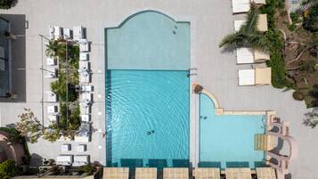 Vista aérea de uma piscina com espreguiçadeiras e uma pequena cascata.