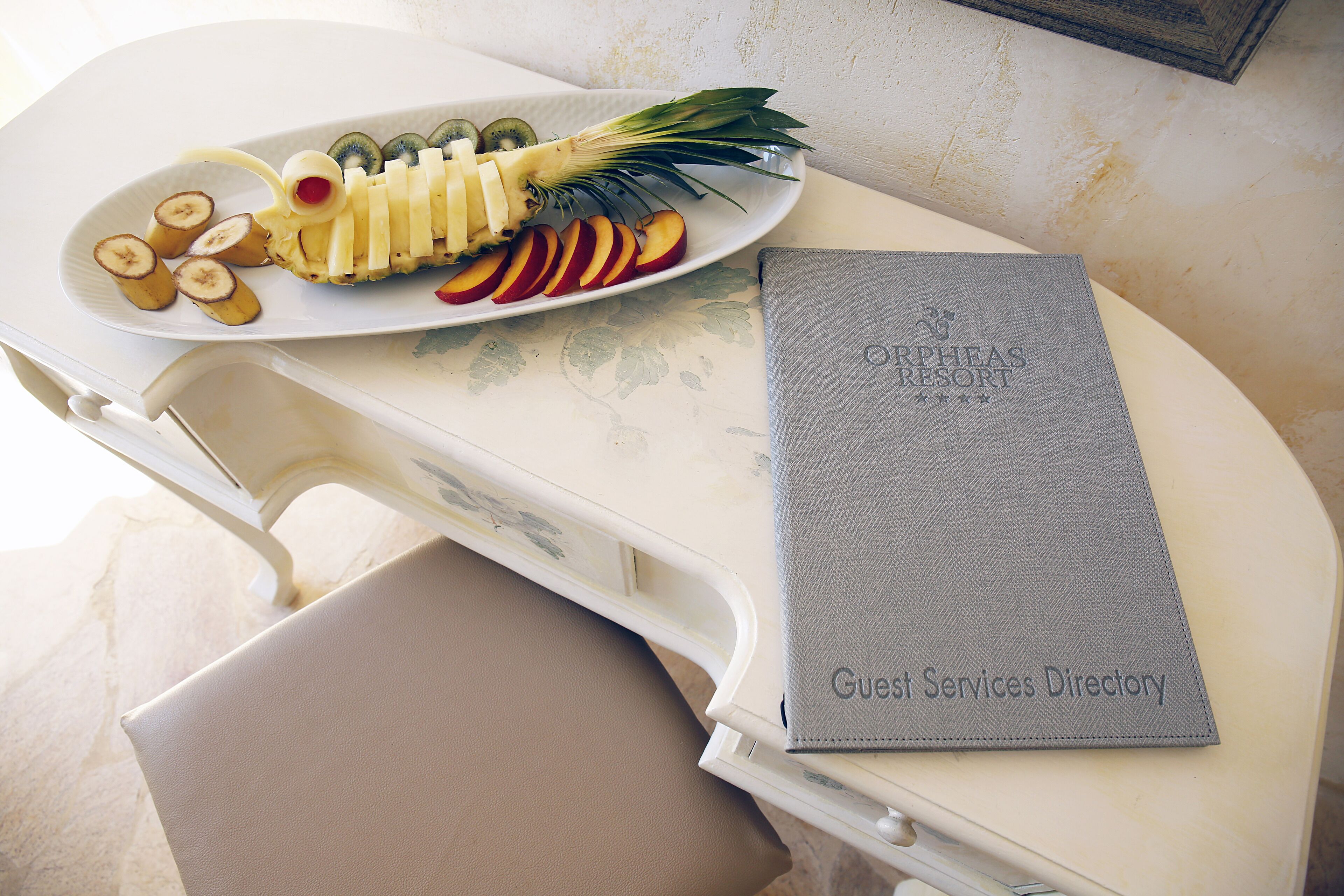 A white table with a plate of sliced fruits and a guest services directory.