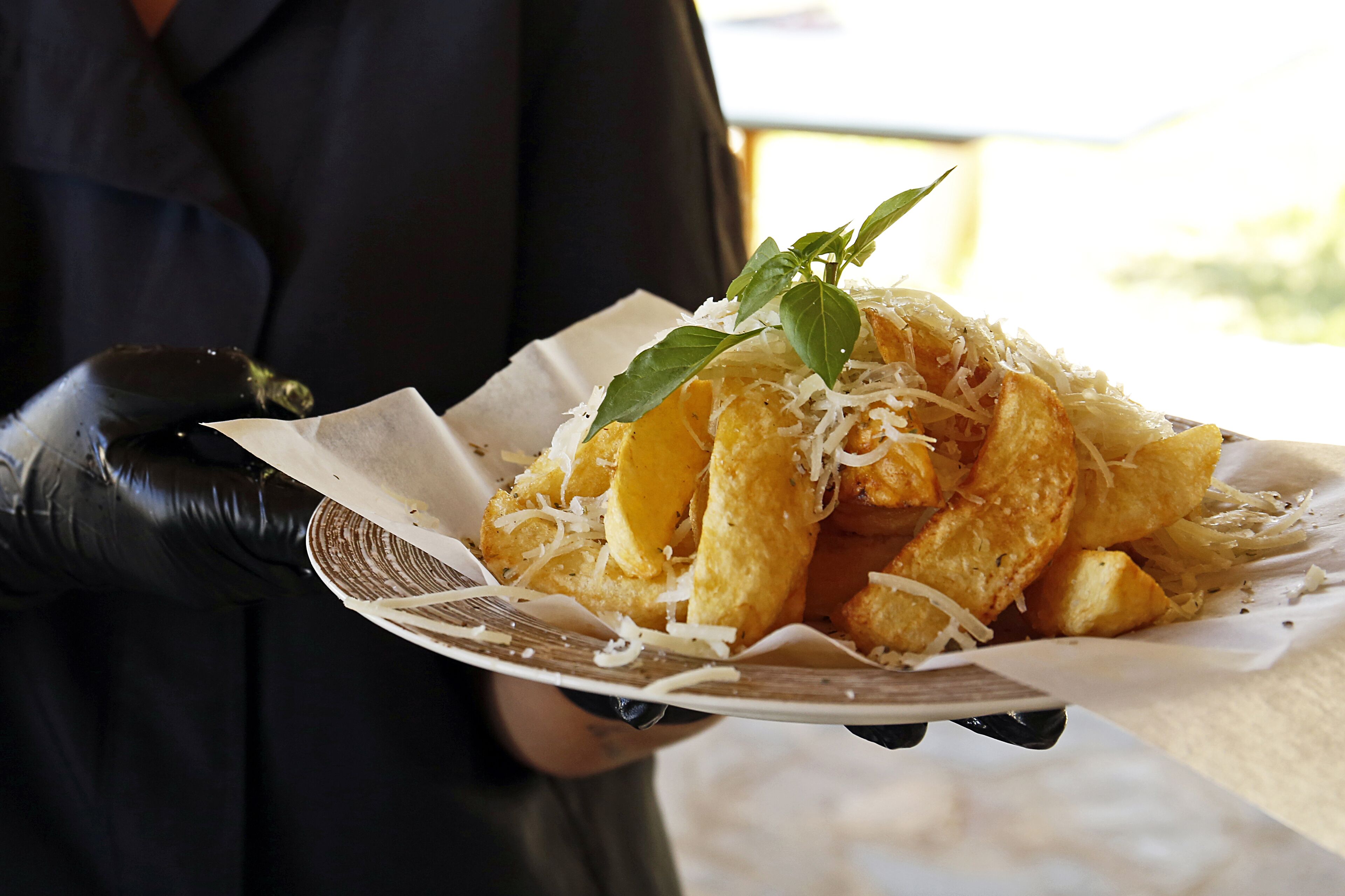 Una persona sosteniendo un plato de comida con papas fritas y queso, decorado con una hoja.