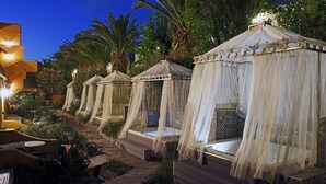 A row of four canopy-style outdoor sleeping areas with steps leading up to them, surrounded by lush greenery and a stone pathway. - Orpheas Resort - Adults Only (Apokoronas)
