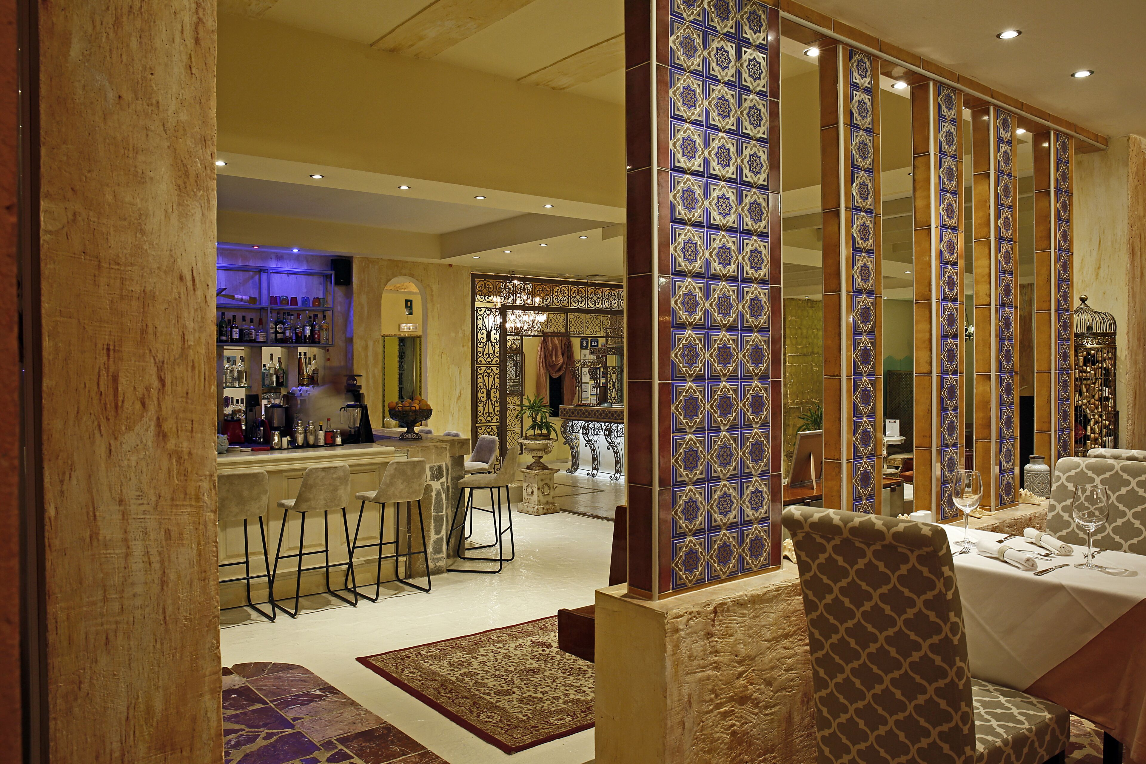 A bar area with stools, a counter with various bottles, and a seating area with patterned chairs.