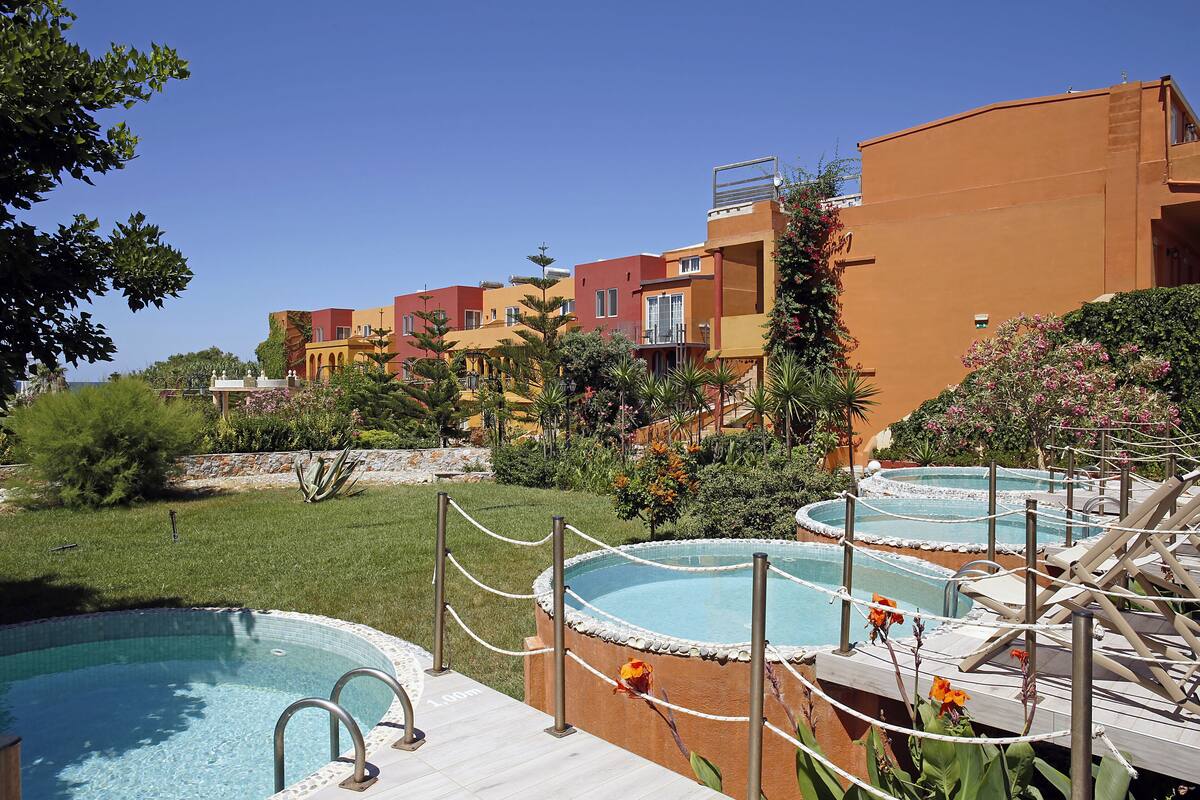 A pool area with multiple hot tubs, a wooden deck, and a backdrop of colorful buildings.