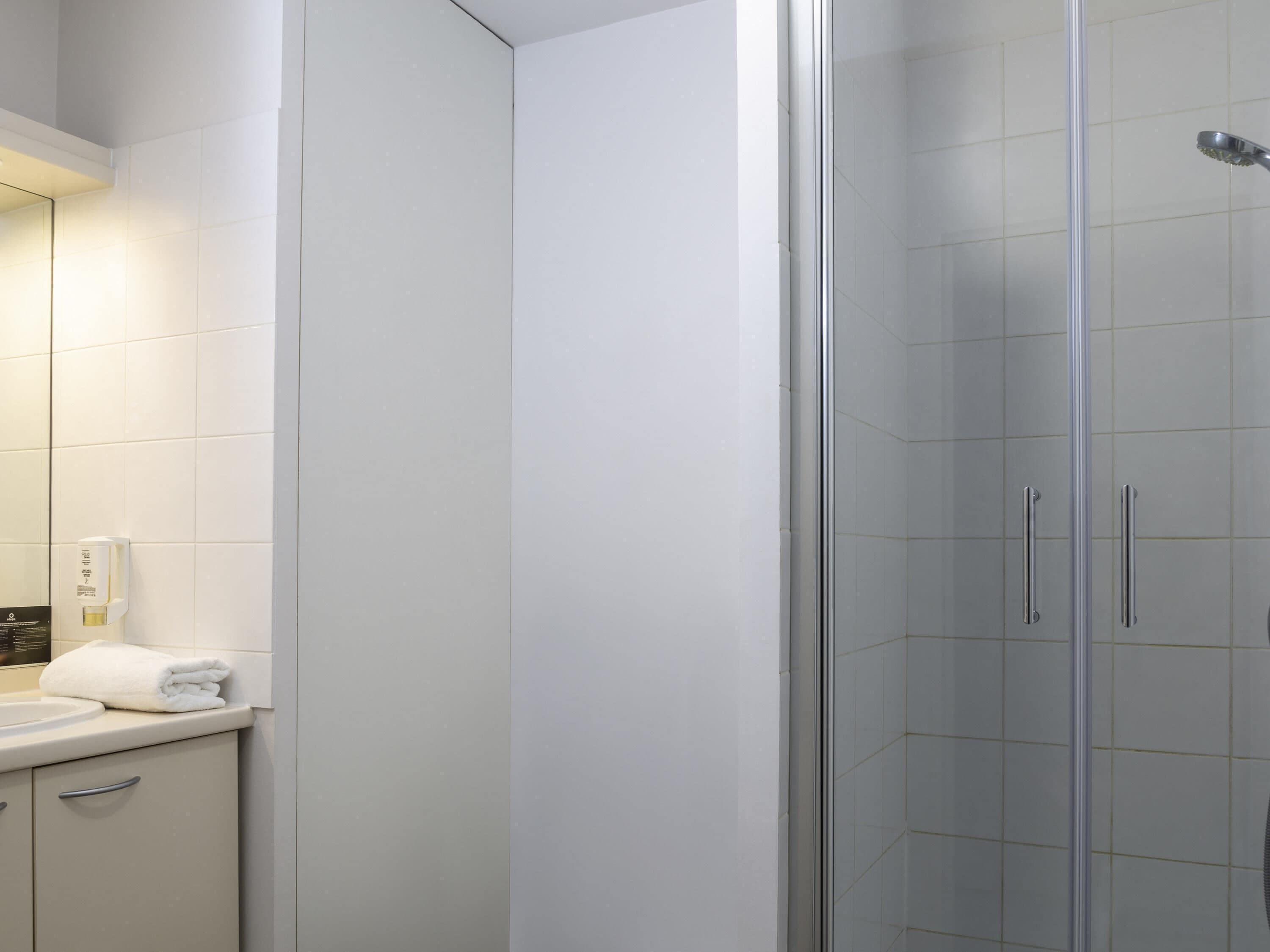 A modern bathroom with a glass shower enclosure, a white sink, and a towel rack.