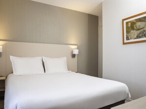 A neatly made bed with white linens, a headboard, and two wall-mounted bedside lamps.