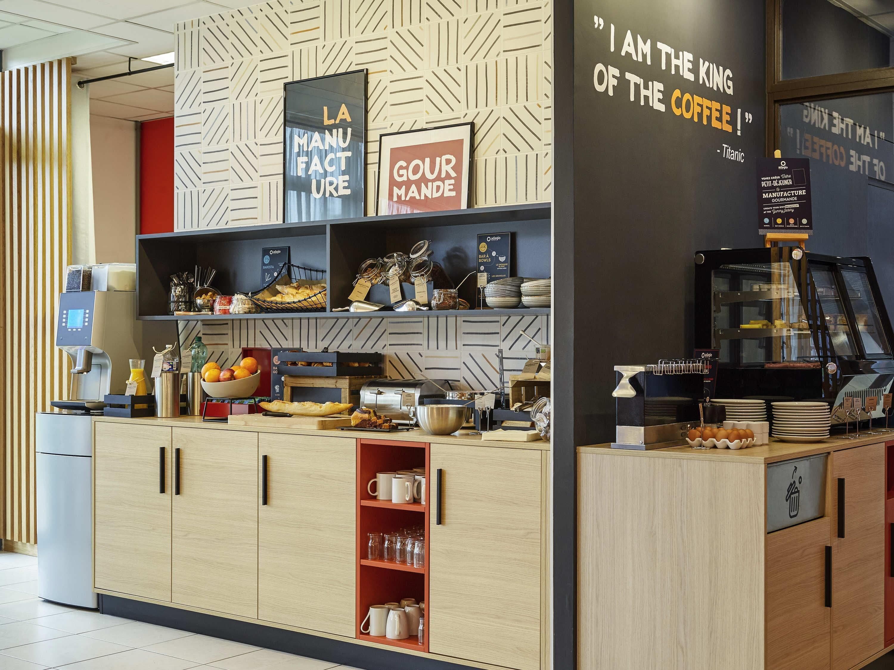 Eine Theke eines Cafés mit einer Kaffeemaschine, Regale voller Gebäck und ein Schild mit der Aufschrift 'I AM THE KING OF THE COFFEE'.