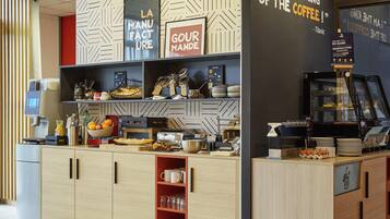Eine Theke eines Cafés mit einer Kaffeemaschine, Regale voller Gebäck und ein Schild mit der Aufschrift 'I AM THE KING OF THE COFFEE'.