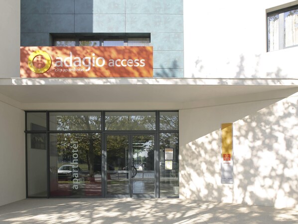 A modern building entrance with glass doors, a sign reading 'adagio access city apart hotel,' and a reflection of trees in the glass. - Aparthotel Adagio Access Avignon (Avignon)