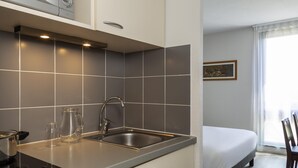 Cozinha moderna com pia, fogão e armários. Uma cama e uma área de refeições são visíveis ao fundo.