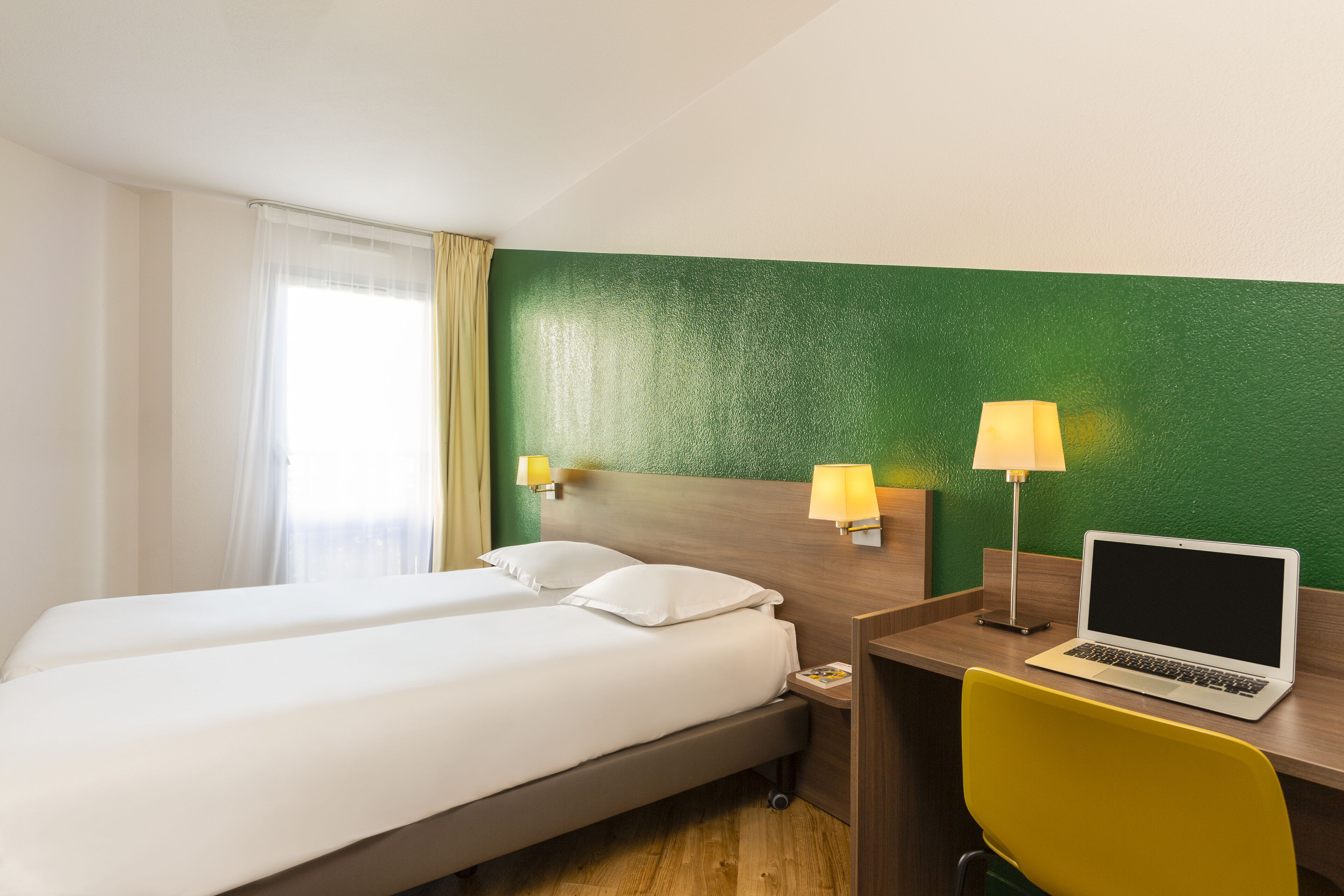 Habitación de hotel con dos camas, un escritorio con una computadora portátil y dos lámparas de pared.