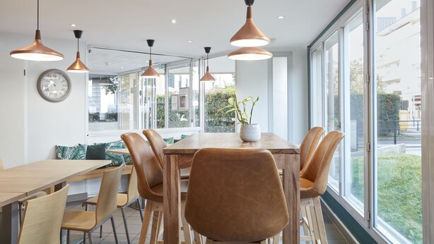 A modern dining area with a wooden table, leather chairs, and pendant lighting. - Aparthotel Adagio Access Carrières-sous-Poissy (Carrieres-sous-Poissy)