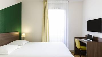 Une chambre d’hôtel avec un lit, un bureau avec un ordinateur portable, une chaise, un téléviseur fixé au mur et une fenêtre avec des rideaux.