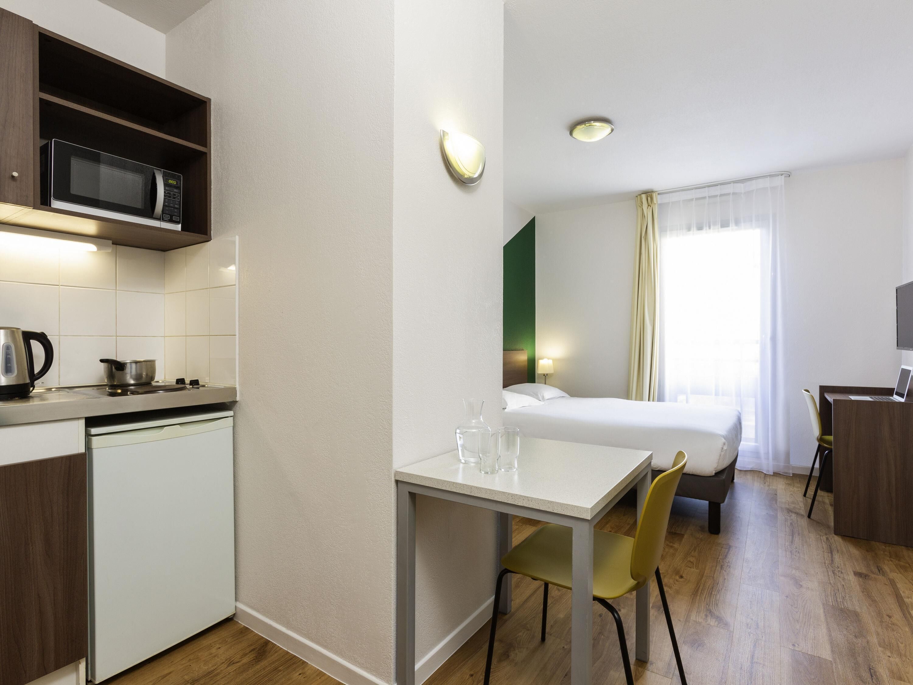 A compact hotel room with a kitchenette, a bed, a desk, and a TV.