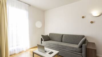 A modern living room with a grey sofa, a small table with a laptop, and a smartphone.