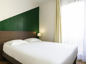 A hotel room with a bed, a nightstand, a lamp, and a window with curtains.