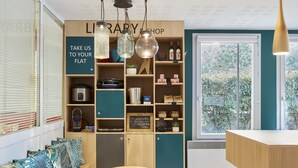 A cozy library and shop area with wooden shelves, a chalkboard menu, and a view of greenery outside. - Aparthotel Adagio Access Carrières-sous-Poissy (Carrieres-sous-Poissy)