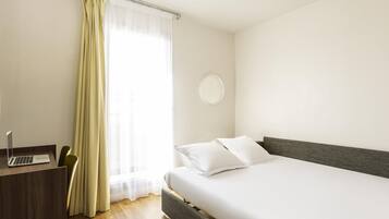 A hotel room with a bed, a desk with a laptop, a chair, and a window with curtains.