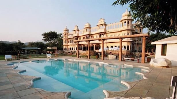 A large pool with a unique shape, surrounded by a building with traditional architecture, including domes and arches. - Fateh Bagh (Desuri)