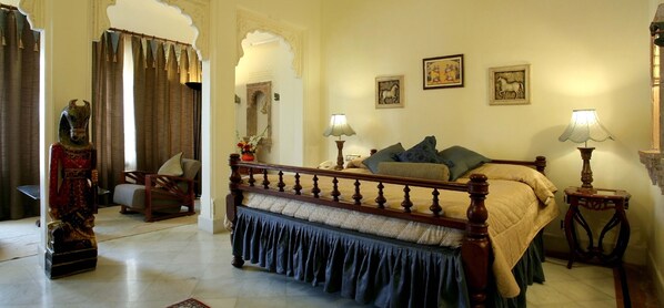 A traditional bedroom with a wooden bed, two bedside tables with lamps, a mirror, and artwork on the walls.