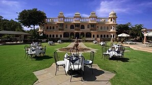 A large, ornate building with a central fountain, surrounded by a well-maintained lawn and outdoor seating areas. - Fateh Bagh (Desuri)