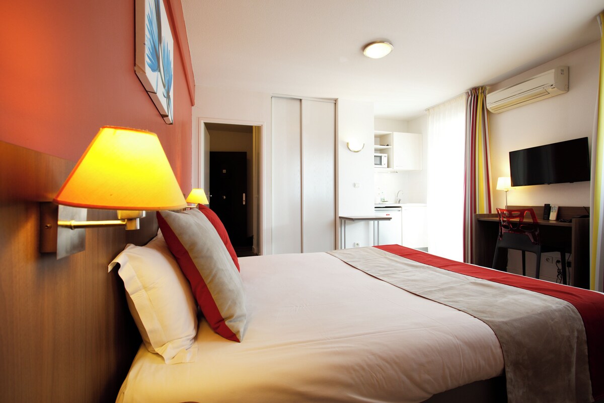 A hotel room with a bed, a desk, a chair, a TV, and a microwave.