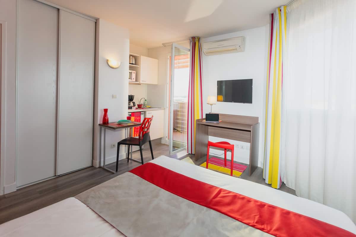 Habitació d'hotel amb llit, escriptori, cadira, televisió i petita cuina.