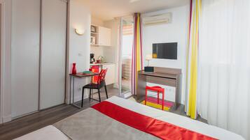 Habitación de hotel con cama, escritorio, silla, televisión y kitchenette.